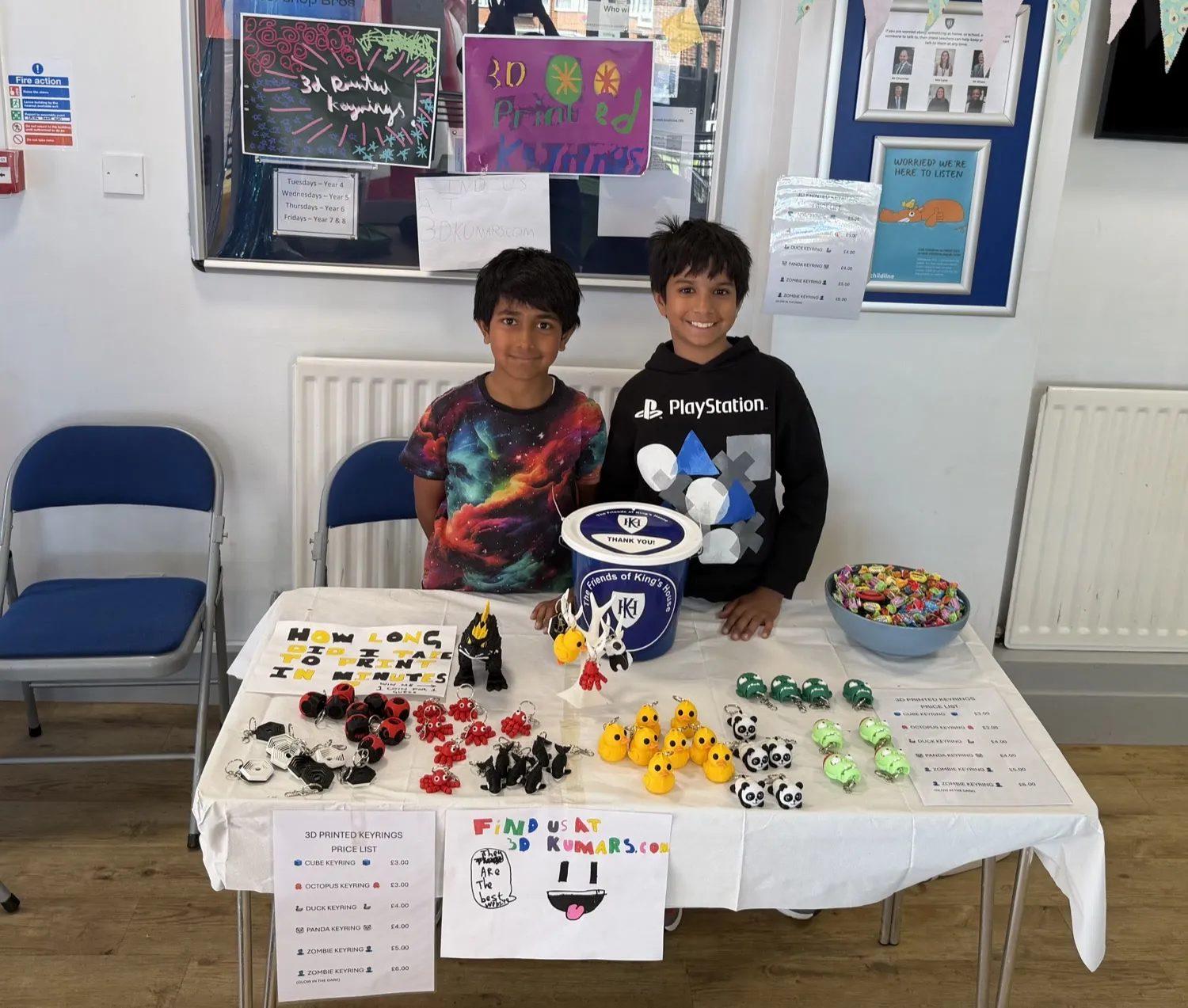 Aaryan and Ayden at their 3D Kumars stall at the Kings House fair, with keyrings and the guess-the-print-time competition